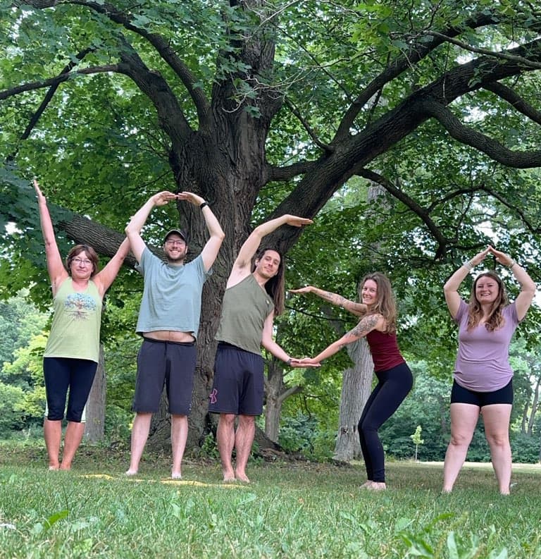 Yoga students posing together outdoors beneath a tree